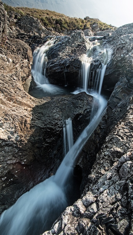 Small waterfall flowing into a clear Fairy Pool with mossy rocks
